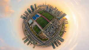A 360° tiny planet aerial view showing a main green football field alongside smaller pitches and padel courts By Forsan Alamal Alsarea